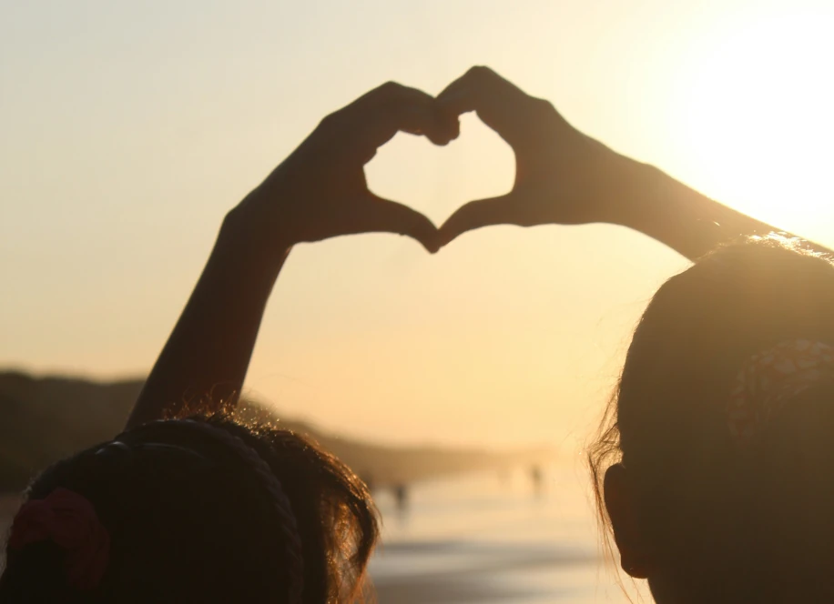 Deux mains qui forment un coeur face à un coucher de soleil