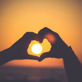 Deux mains qui font un cœur avec un coucher de soleil derrière